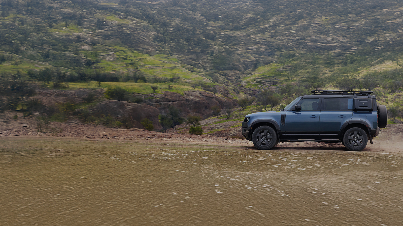 Side view of a blue Defender driving through rolling green hills with promotional text overlay stating 'Up to £4,204 savings and 6.9% APR'.