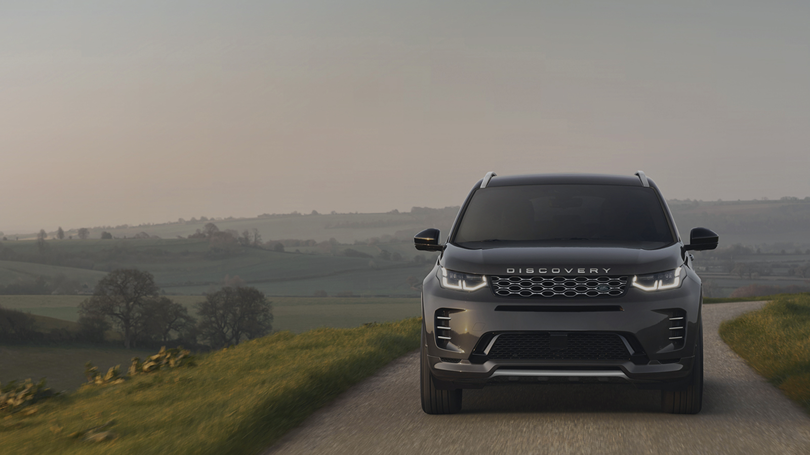 Front view of a Discovery Sport, driving on a road surrounded by hills with promotional text overlay stating 'Up to £2,688 savings and 6.9% APR'.