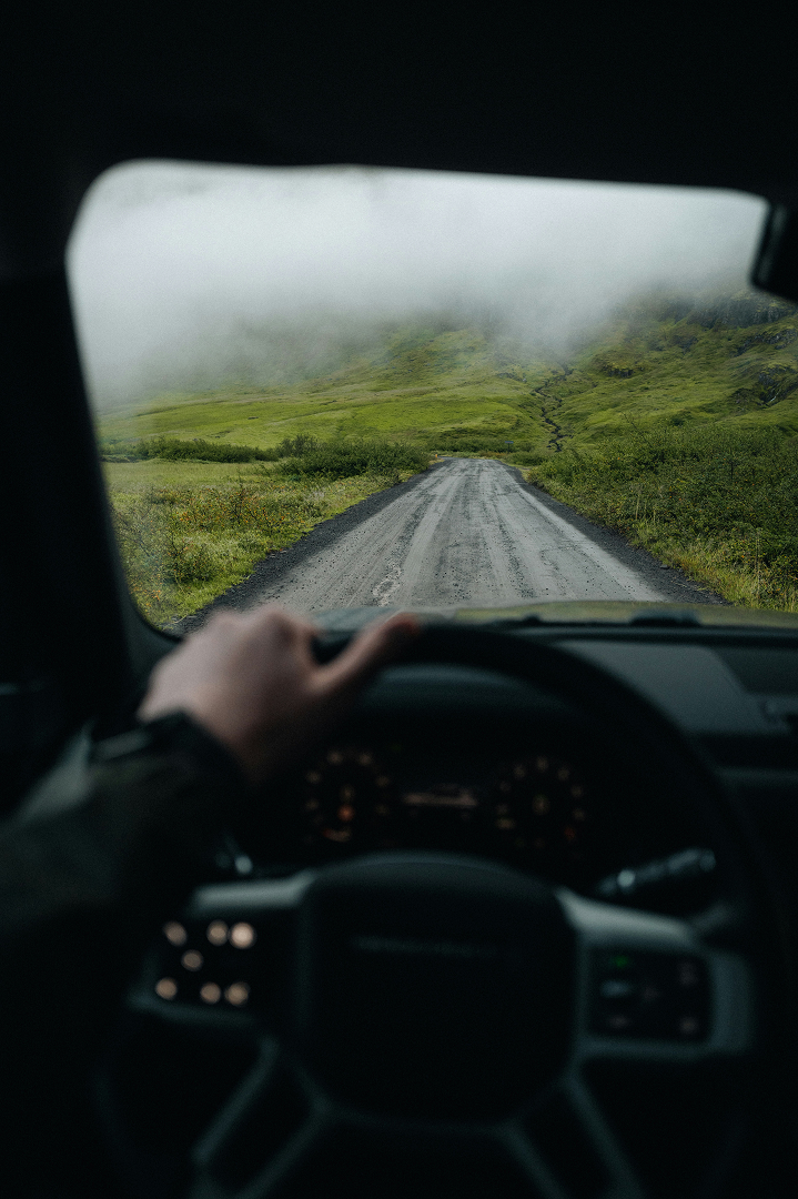 Point-of-view of driving a Land Rover on a foggy day, surrounded by green hills.