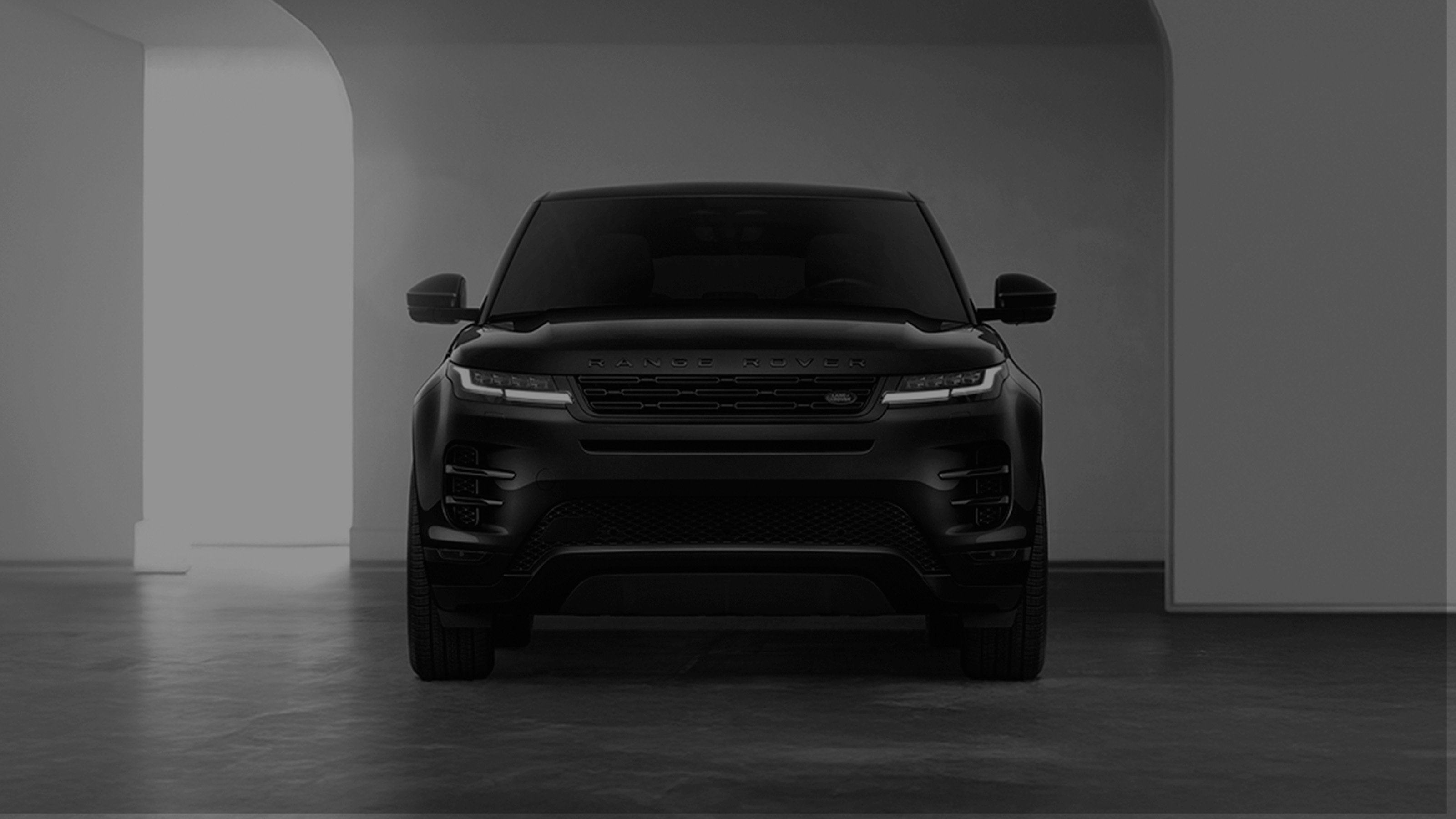 Front view of a black Range Rover Evoque parked in a modern, minimalistic indoor space with promotional text overlay.